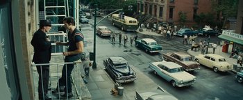 Movie still from “West Side Story” (2021), directed by Steven Spielberg – A street scene with cars and people walking on the sidewalk; Wide shot, High angle