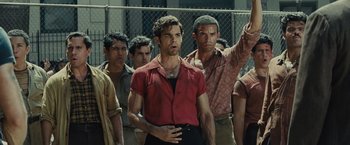 Movie still from “West Side Story” (2021), directed by Steven Spielberg – A group of men standing next to each other in front of a chain link fence; Medium shot, Low angle