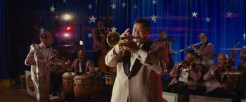 Movie still from “West Side Story” (2021), directed by Steven Spielberg – A man playing a trumpet in front of a group of people; Wide shot, Low angle