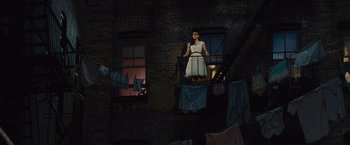 Movie still from “West Side Story” (2021), directed by Steven Spielberg – A woman standing on a balcony next to a window; Wide shot, High angle