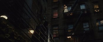 Movie still from “West Side Story” (2021), directed by Steven Spielberg – A woman in a white dress standing on a fire escape; Wide shot, Low angle