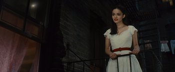 Movie still from “West Side Story” (2021), directed by Steven Spielberg – A woman in a white dress standing next to a railing; Medium shot, Over the shoulder angle