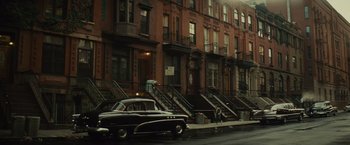 Movie still from “West Side Story” (2021), directed by Steven Spielberg – A car parked on the side of the road next to a row of buildings; Extreme Wide shot, High angle