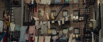Movie still from “West Side Story” (2021), directed by Steven Spielberg – A woman in a yellow dress standing on the balcony of an apartment building; Extreme Wide shot, Overhead angle