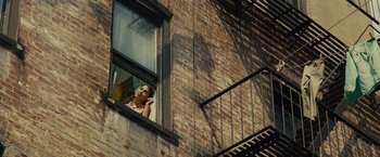Movie still from “West Side Story” (2021), directed by Steven Spielberg – A woman looking out of a window on a brick building; Wide shot, Low angle