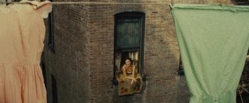 Movie still from “West Side Story” (2021), directed by Steven Spielberg – A woman sitting on a window ledge looking out of a window; Wide shot, Overhead angle