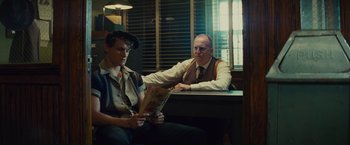 Movie still from “West Side Story” (2021), directed by Steven Spielberg – A man sitting next to another man holding a newspaper; Medium shot, Over the shoulder angle