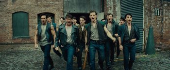 Movie still from “West Side Story” (2021), directed by Steven Spielberg – A group of men in leather jackets holding a baseball bat; Medium shot, Low angle