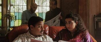 Movie still from “What's Love Got to Do with It?” (2022), directed by Shekhar Kapur – A man and a woman sitting next to each other on a couch; Medium shot, Over the shoulder angle