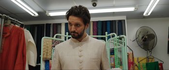 Movie still from “What's Love Got to Do with It?” (2022), directed by Shekhar Kapur – A man in a suit stands next to a rack; Medium shot, Over the shoulder angle