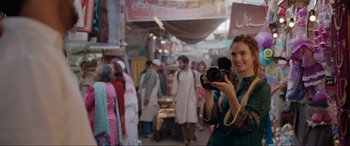 Movie still from “What's Love Got to Do with It?” (2022), directed by Shekhar Kapur – A woman is holding a camera in the middle of a crowded street; Medium shot, Over the shoulder angle