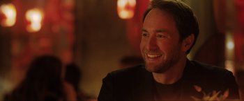 Movie still from “What's Love Got to Do with It?” (2022), directed by Shekhar Kapur – A man smiling while sitting at a table in a restaurant; Close Up shot, Over the shoulder angle