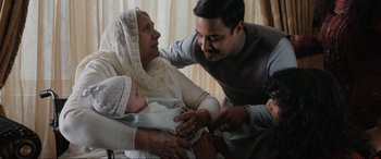 Movie still from “What's Love Got to Do with It?” (2022), directed by Shekhar Kapur – An older woman holding a baby while a young man holds it; Medium shot, Over the shoulder angle