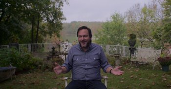 Movie still from “White Hot: The Rise & Fall of Abercrombie & Fitch” (2022), directed by Alison Klayman – A man sitting on a chair in a yard; Medium shot, High angle