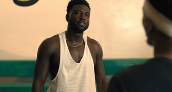 Movie still from “White Men Can't Jump” (2023), directed by Calmatic – A man in a white tank top looking at the camera; Medium shot, Over the shoulder angle