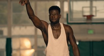Movie still from “White Men Can't Jump” (2023), directed by Calmatic – A man in a white tank top raises his fist; Medium shot, Low angle