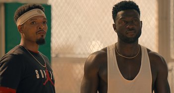 Movie still from “White Men Can't Jump” (2023), directed by Calmatic – Two men standing next to each other in front of a chain link fence; Close Up shot, Over the shoulder angle
