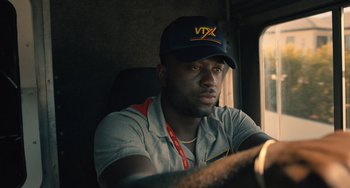 Movie still from “White Men Can't Jump” (2023), directed by Calmatic – A man sitting in a vehicle wearing a hat; Close Up shot, Low angle