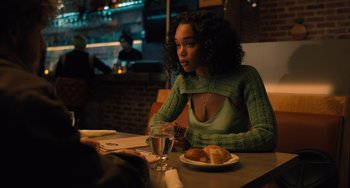 Movie still from “White Men Can't Jump” (2023), directed by Calmatic – A woman sitting at a table with a plate of food; Medium shot, Over the shoulder angle