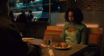 Movie still from “White Men Can't Jump” (2023), directed by Calmatic – A woman sitting at a table in front of a plate of food; Medium shot, Over the shoulder angle