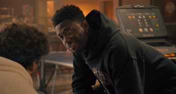 Movie still from “White Men Can't Jump” (2023), directed by Calmatic – A person wearing a hoodie smiling; Close Up shot, Over the shoulder angle