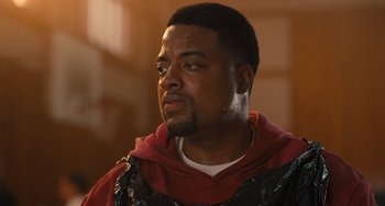 Movie still from “White Men Can't Jump” (2023), directed by Calmatic – A man in a red and black shirt looking to his left; Close Up shot, Low angle