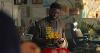 Movie still from “White Men Can't Jump” (2023), directed by Calmatic – A man sitting in front of a wall holding a pair of shoes; Close Up shot, Over the shoulder angle