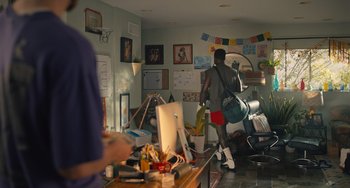 Movie still from “White Men Can't Jump” (2023), directed by Calmatic – A man walking through a cluttered living room; Wide shot, Over the shoulder angle