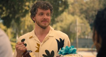 Movie still from “White Men Can't Jump” (2023), directed by Calmatic – A man with a beard is holding a bottle of wine and a cake; Close Up shot, Over the shoulder angle