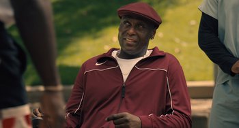 Movie still from “White Men Can't Jump” (2023), directed by Calmatic – A man wearing a maroon jacket and a hat; Medium shot, Over the shoulder angle
