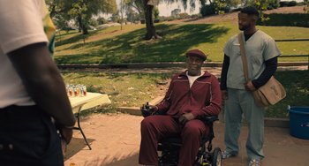 Movie still from “White Men Can't Jump” (2023), directed by Calmatic – A man sitting in a wheel chair next to a table; Wide shot, High angle