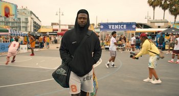 Movie still from “White Men Can't Jump” (2023), directed by Calmatic – A man standing on a basketball court holding a bag; Medium shot, Over the shoulder angle
