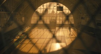Movie still from “White Men Can't Jump” (2023), directed by Calmatic – A person standing in front of a window in a gym; Extreme Wide shot, Low angle