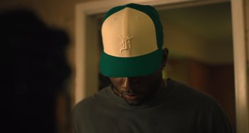 Movie still from “White Men Can't Jump” (2023), directed by Calmatic – A man wearing a green and white hat; Close Up shot, Over the shoulder angle