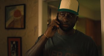 Movie still from “White Men Can't Jump” (2023), directed by Calmatic – A man wearing a hat talking on a cell phone; Close Up shot, Low angle