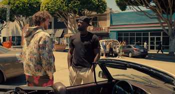 Movie still from “White Men Can't Jump” (2023), directed by Calmatic – A man standing next to a car on a street; Medium shot, Over the shoulder angle
