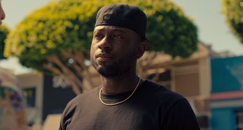 Movie still from “White Men Can't Jump” (2023), directed by Calmatic – A man wearing a black hat and a black t - shirt; Close Up shot, Low angle
