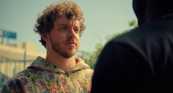 Movie still from “White Men Can't Jump” (2023), directed by Calmatic – A man with curly hair wearing a floral shirt; Close Up shot, Over the shoulder angle