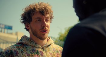 Movie still from “White Men Can't Jump” (2023), directed by Calmatic – A man with curly brown hair wearing a floral shirt talking to another man; Close Up shot, Over the shoulder angle
