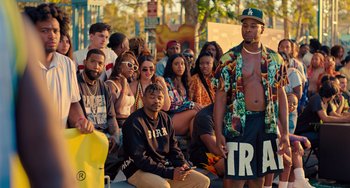 Movie still from “White Men Can't Jump” (2023), directed by Calmatic – A group of young people sitting on the side of the street; Wide shot, Over the shoulder angle