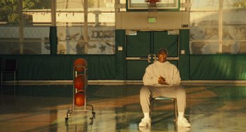 Movie still from “White Men Can't Jump” (2023), directed by Calmatic – A man sitting on a chair in a gym; Wide shot, High angle