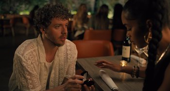 Movie still from “White Men Can't Jump” (2023), directed by Calmatic – A man sitting at a table looking at a cell phone; Medium shot, Over the shoulder angle