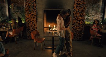 Movie still from “White Men Can't Jump” (2023), directed by Calmatic – A man and a woman kissing in front of a fireplace; Wide shot, Over the shoulder angle