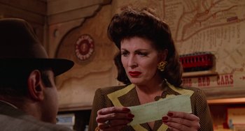 Movie still from “Who Framed Roger Rabbit” (1988), directed by Robert Zemeckis – A woman in a yellow and brown suit holding a piece of paper; Close Up shot, Over the shoulder angle