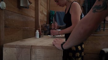 Movie still from “Wildcat” (2022), directed by Melissa Lesh – A woman in a black top is cutting paper with scissors; Medium shot, High angle