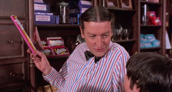 Movie still from “Willy Wonka & the Chocolate Factory” (1971), directed by Mel Stuart – A man in striped shirt and bow tie holding a knife; Medium shot, Over the shoulder angle