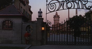 Movie still from “Willy Wonka & the Chocolate Factory” (1971), directed by Mel Stuart – A clock tower in the distance behind a wrought iron gate; Wide shot, Low angle