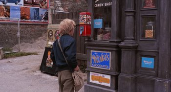 Movie still from “Willy Wonka & the Chocolate Factory” (1971), directed by Mel Stuart – A woman standing in front of a store on the sidewalk; Medium shot, Over the shoulder angle