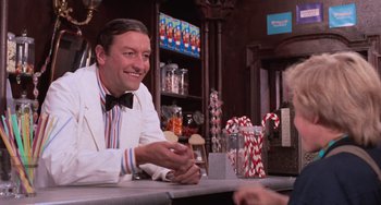 Movie still from “Willy Wonka & the Chocolate Factory” (1971), directed by Mel Stuart – A man sitting at a bar smiling for the camera; Medium shot, Over the shoulder angle
