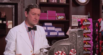 Movie still from “Willy Wonka & the Chocolate Factory” (1971), directed by Mel Stuart – A man wearing a white suit and bow tie in a candy store; Medium shot, Over the shoulder angle